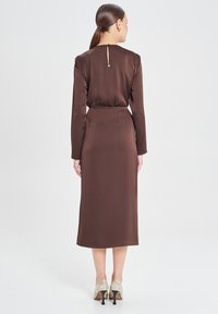 Braunes Satin-Kleid mit langen �Ärmeln, einem Schlüsselverschluss auf der Rückseite und einer taillierten Taille. Der Rock reicht bis zur Mitte der Waden.