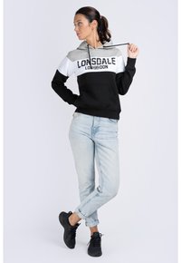 Huvtröja i grått, vitt och svart med en stor logotyp. Matchad med ljusblå upprullade jeans och svarta sneakers. Slät tygkvalitet.