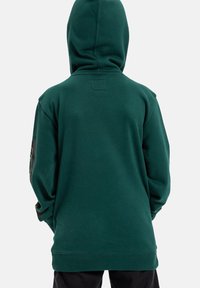 Ciemnozielona bluza z kapturem, z kieszenią typu kangur, sznurkiem przy kapturze oraz ściągaczem na dole. Charakteryzuje się minimalnym wykończeniem na rękawach i plecach. Miękka tekstura materiału.