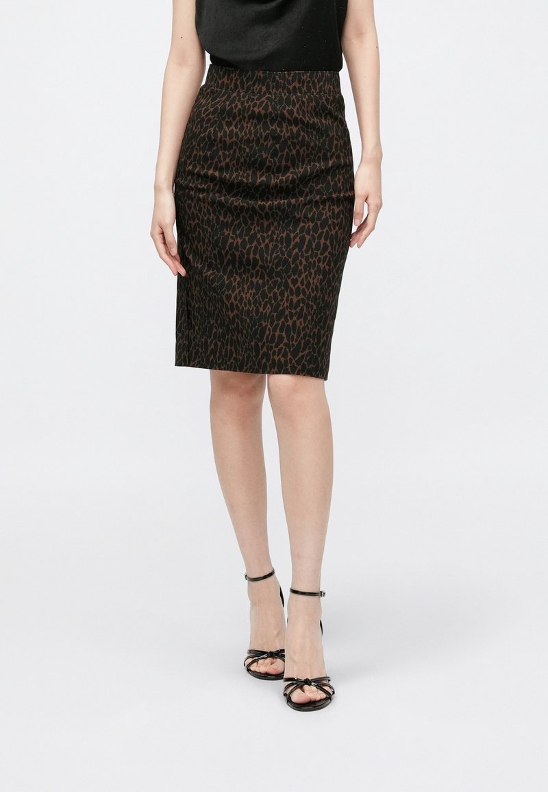 Femme portant une jupe ajustée marron et noire à imprimé animal jusqu'au genou, des sandales noires à talons hauts avec des brides et un haut noir.