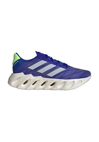 Sneaker sportivo blu con tre strisce bianche, linguetta verde e suola bianca scolpita con fori ovali.