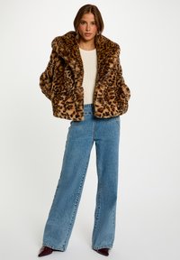 Giacca in pelliccia sintetica con stampa leopardata e ampio colletto, abbinata a jeans in denim blu a vita alta e dal taglio morbido, e tacchi a punta bordeaux.