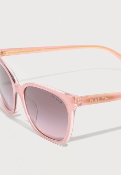 Ροζ διαφανή γυαλιά ηλίου με τετράγωνους φακούς γκρι διαβάθμισης και την επωνυμία "RALPH" στον βραχίονα και τη γωνία του φακού.
