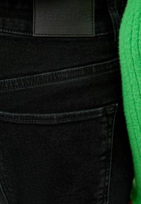 Svarta denimjeans med texturerad yta och synliga sömmar, med en svart etikett präglad med "Bershka" på midjan.