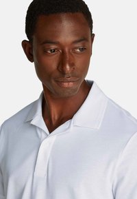 Polo bianco con colletto a bottoni, tessuto texturizzato e un sottile logo del marchio impresso sul colletto.