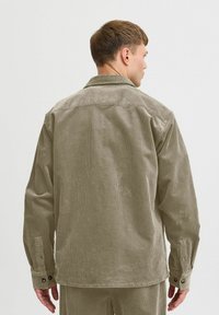 Oliven grøn corduroy skjortejakke med krave, lange ærmer og knaplukning ved manchetterne, med en struktureret fold og en afslappet pasform.