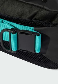 Sort taske med et turkist rem og en sort spænde, med et struktureret mesh-panel nedenunder til ventilation.