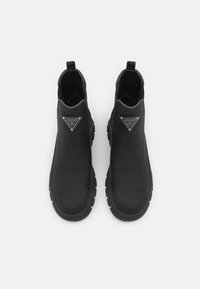 Paire de bottines noires à semelles épaisses avec logo triangulaire Guess sur le devant supérieur, sur fond blanc.