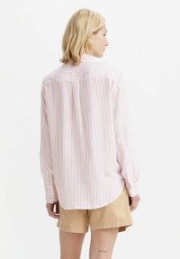 Camicia a maniche lunghe rosa e bianca a righe, con orlo curvo, polsini con bottoni e yoke posteriore, abbinata a pantaloni corti beige.