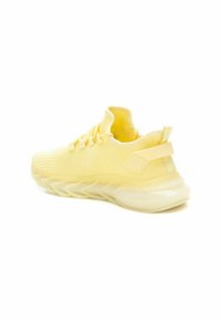 Zapatillas deportivas amarillas con parte superior de malla, punta redonda y suela gruesa y ondulada. Presentan una lengüeta sólida en el talón y detalles texturizados en los laterales.