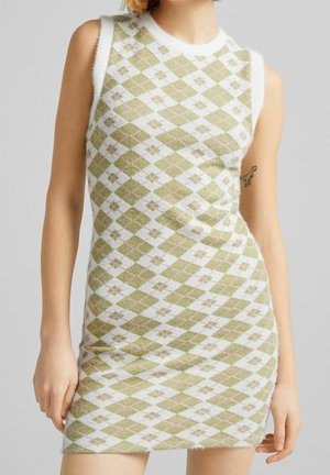 Ärmelloses, figurbetontes Kleid mit grünem und weißem Argyle-Muster und kleinen Blumenmotiven, getragen von einer Person mit einem kleinen Dinosaurier-Tattoo am Arm.