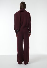 Bordeaux gebreide tweedelige set met een slouchy coltrui en wijde broek, gekenmerkt door een zachte textuur en een ontspannen pasvorm.