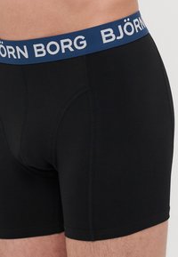 Schwarze Boxershorts aus elastischem Stoff mit einem marineblauen Bund, auf dem der Markenname "BJÖRN BORG" in weißen Buchstaben erscheint.