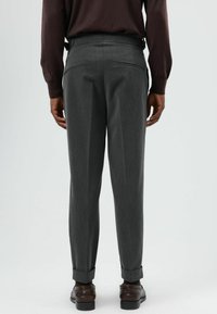 Grijze pantalon met rechte pijpen, voorzien van twee achterzakken en omgeslagen boorden. De stof heeft een subtiele textuur; gedragen met bruine schoenen.