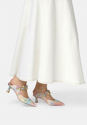 Pies con zapatos de tacón bajo en tonos pastel, puntera en pico, con tiras adornadas con joyas, combinados con una falda larga blanca y fluida o vestido.