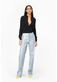 Camicia nera con bottoni, jeans a palazzo metallici blu chiaro e décolleté gialli a punta. Texture lisce e dettagli in vita aderenti.