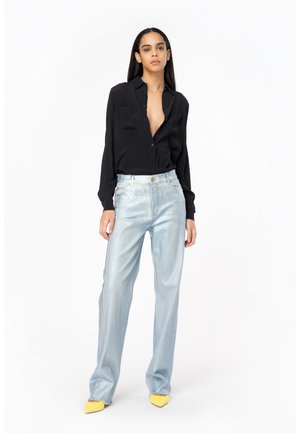 Camicia nera con bottoni, jeans a palazzo metallici blu chiaro e décolleté gialli a punta. Texture lisce e dettagli in vita aderenti.