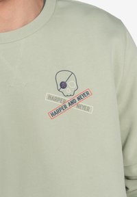 Sudadera verde claro con cuello redondo. Presenta un esqueleto bordado y el texto "HARPER AND NEVER" en colores contrastantes.