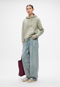 Lysegrønn hettegenser med frontlommer, parret med vide lyseblå jeans. Sølv sneakers og en mørk burgunder quiltet veske fullfører antrekket.