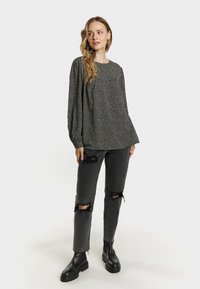 Blouse noire à manches longues avec un motif à pois, associée à un jean gris déchiré et des bottes noires chunky.