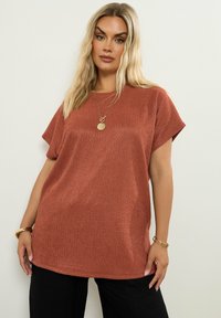 Ruskvärgad kortärmad topp med en strukturerad ribbad textile. Avslappnad passform, rund halsringning och sidoflärpar för ökad rörelsefrihet.