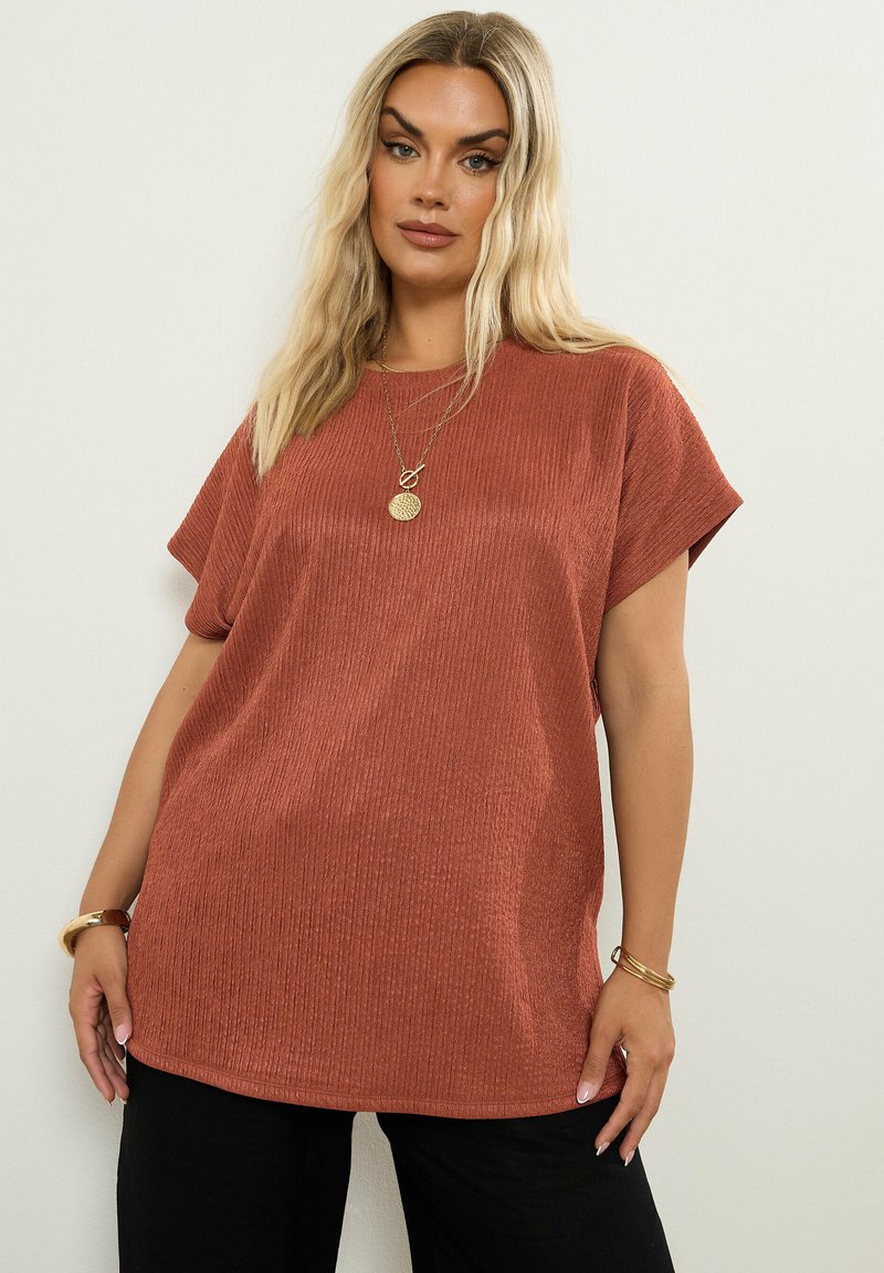 Ruskvärgad kortärmad topp med en strukturerad ribbad textile. Avslappnad passform, rund halsringning och sidoflärpar för ökad rörelsefrihet.