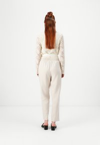 Blonde bluse med lange ærmer i creme, parret med lysebeige tapered bukser. Materialet ser blødt ud; blusen har en tætsiddende talje og delikate detaljer.