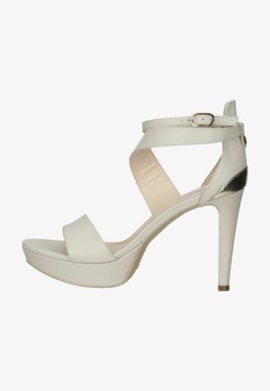 Weiße High-Heel-Sandale mit glänzender Oberfläche, Knöchelriemen, Kreuzriemen-Design, Plattformsohle und metallischem Akzent am Absatz.