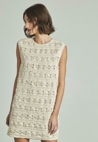 Ärmelloses Spitzenstrickkleid in hellem Beige, mit einem strukturierten Muster mit runden Details und einem runden Ausschnitt.