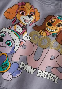 Lys lilla genser med tegneseriehunder, med teksten "GOOD PUPS PAW PATROL" i en blanding av rosa og skinnende gullbokstaver.