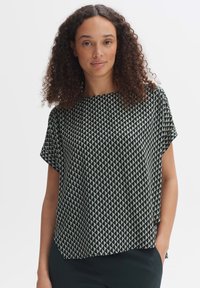 Top nero a maniche corte con un motivo geometrico di triangoli color crema. Tessuto leggero con una vestibilità rilassata e scollo rotondo.