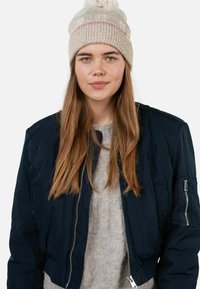 Navy bomber jacket with a zip front, featuring a textured gray sweater underneath and a beige knit beanie with a pom-pom on top.