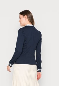 Giacca a maniche lunghe di colore blu navy con colletto e polsini a righe bianche, dotata di una vestibilità su misura e una texture liscia.