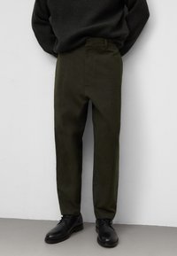 Olijfgroene op maat gemaakte broeken van een gestructureerde stof, met een vlakke voorkant, zijzakken en een slim fit. Gecombineerd met zwarte schoenen.