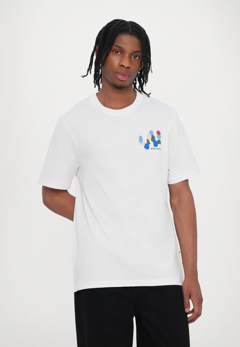 White cotton t-shirt with short sleeves, featuring a multicolored graphic on the left chest, depicting abstract shapes and text.