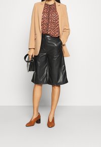 Ljusbrun kavaj, mönstrad rosa topp, svarta fusk läder culotter, bruna klackskor och en svart handväska. Släta texturer, modern design.