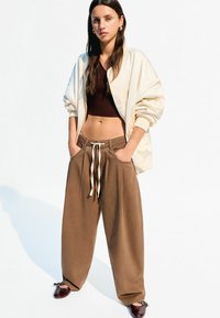 Creme bomberjakke, brun ribbet crop top og løse brune bukser med hvid snøre. Brune sko med accenter. Minimalistisk stil.