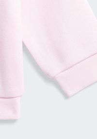 Světlerůžová bavlněná mikinová látka s texturovaným povrchem, s žebrovanými manžetami a čistým lemem. Pohled zhora na detaily rukávu.