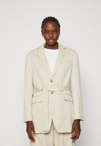 Beige Leinenblazer mit einem Gürtel, zwei vorderen Taschen und einer einfachen Knopfschließe. Taillierte Passform mit Reverskragen und langen Ärmeln.
