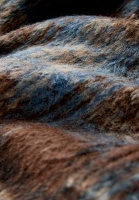 Textured wool fabric in earthy tones of brown and blue, featuring varying strands that create a layered, undulating appearance.