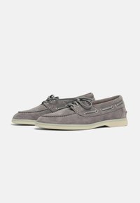Zapatillas de barco de ante gris con textura suave, suela de goma blanca y cordones decorativos con ojales metálicos. Diseñadas para uso casual.