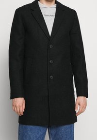 Černý kabát z vlněné směsi s kostkovaným vzorem, jednorušný střih, klopový límec s výřezy a tři přední knoflíky, s bočními kapsami.