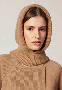 Beige gestrickter Pullover mit integrierter Kapuze, der eine gerippte Textur und einen weiten Kragen aufweist. Glattes, weiches Material mit einem lässigen Design.