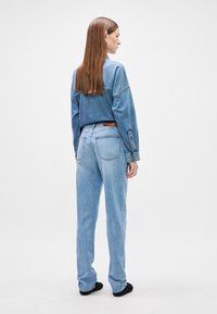 Svetlo modra teksas srajca in hlače z sproščenim krojem. Hlače imajo zadnje žepe in rjavo usnjeno oznako. Gladka tekstura, sproščen dizajn.