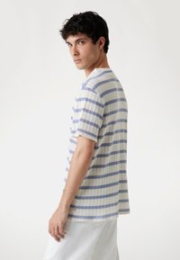 Camiseta de punto a rayas en crema y azul claro. Mangas cortas, cuello redondeado. Presenta un tejido texturizado con patrón visible y ribetes acanalados.