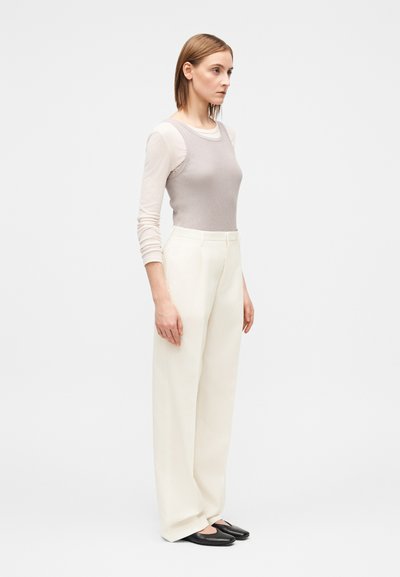 Šviesiai pilkas ribuotas marškinėlių tipo viršus derinamas su aukštu liemeniu baltais kelnėmis. Aprangą papildo juodi lygūs batai su aerodinamišku dizainu.