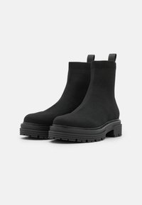 Botas negras de tobillo con parte superior de punto, suela de goma gruesa y tiradores; textura suave con una suela acanalada para mayor agarre.