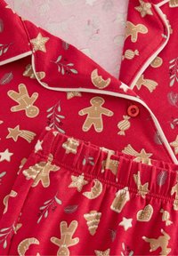 Rode pyjama set met een verscheidenheid aan peperkoekmannetjes en seizoensgebonden iconen. Zacht katoenmateriaal met piping en detail van een elastische tailleband.