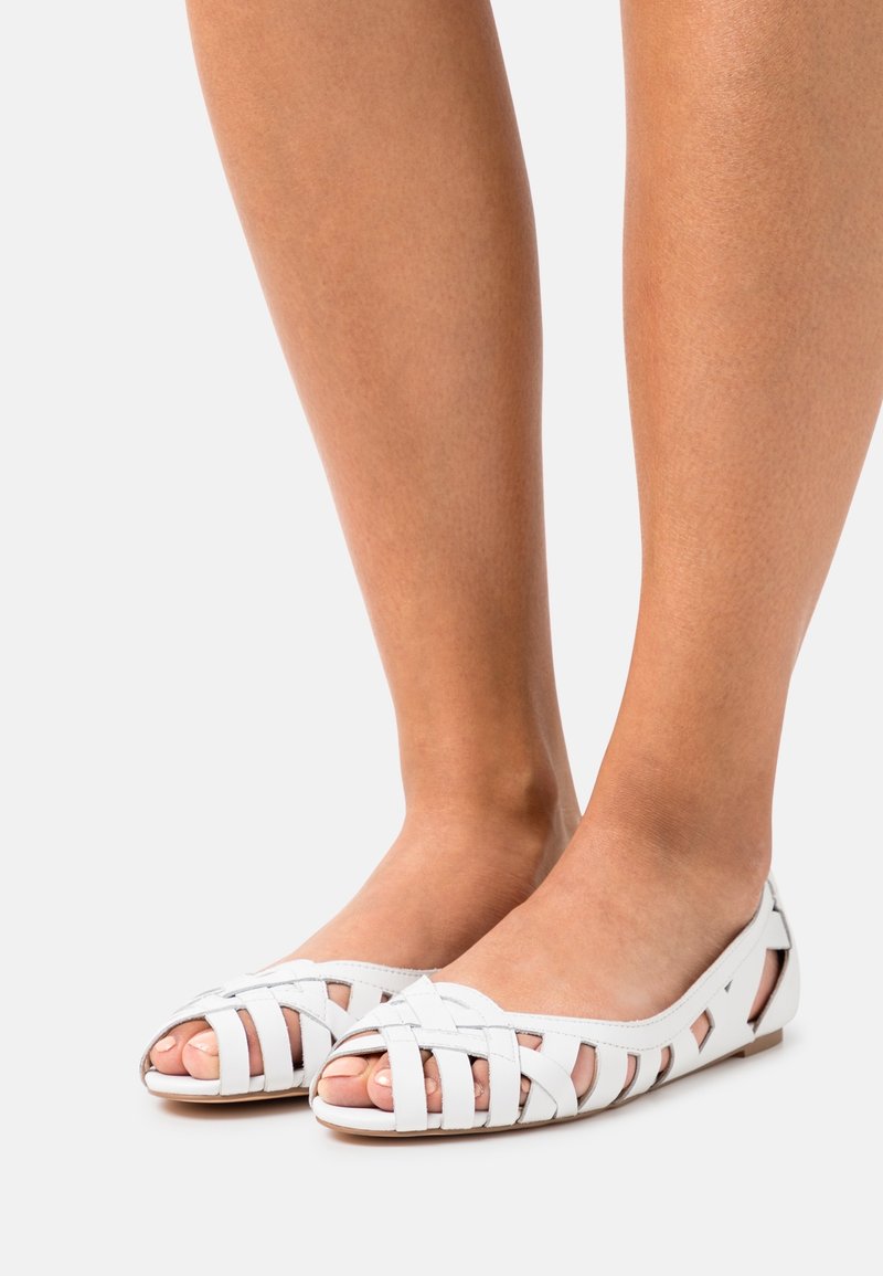 Chaussures plates en cuir blanc avec un design à bout ouvert, dotées de brides tissées et d'une semelle plate. Texture lisse avec des détails découpés.