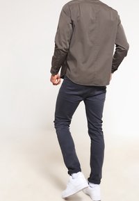 Camicia verde scuro con maniche lunghe, abbinata a jeans grigi scuri slim-fit e sneakers bianche. Tessuto morbido con dettagli minimi.